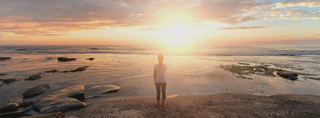 Girl on beach against a rising sun over still waters evoking a symbolic view of a safe bright and secure future.